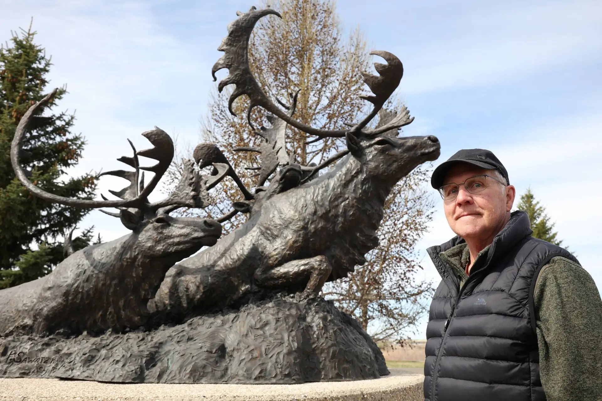 Sculptor Peter Sawatzky in front of his bronze sculpture of caribou crossing a river